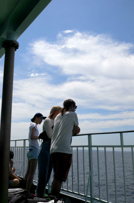 フェリーの甲板から海を眺める外国人観光客